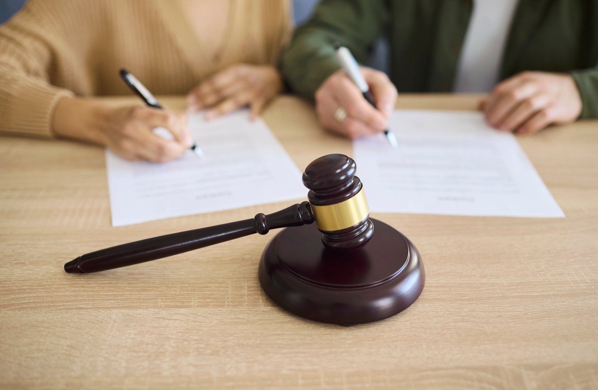 Two people sitting at a desk signing paperwork in front of a judges gavel