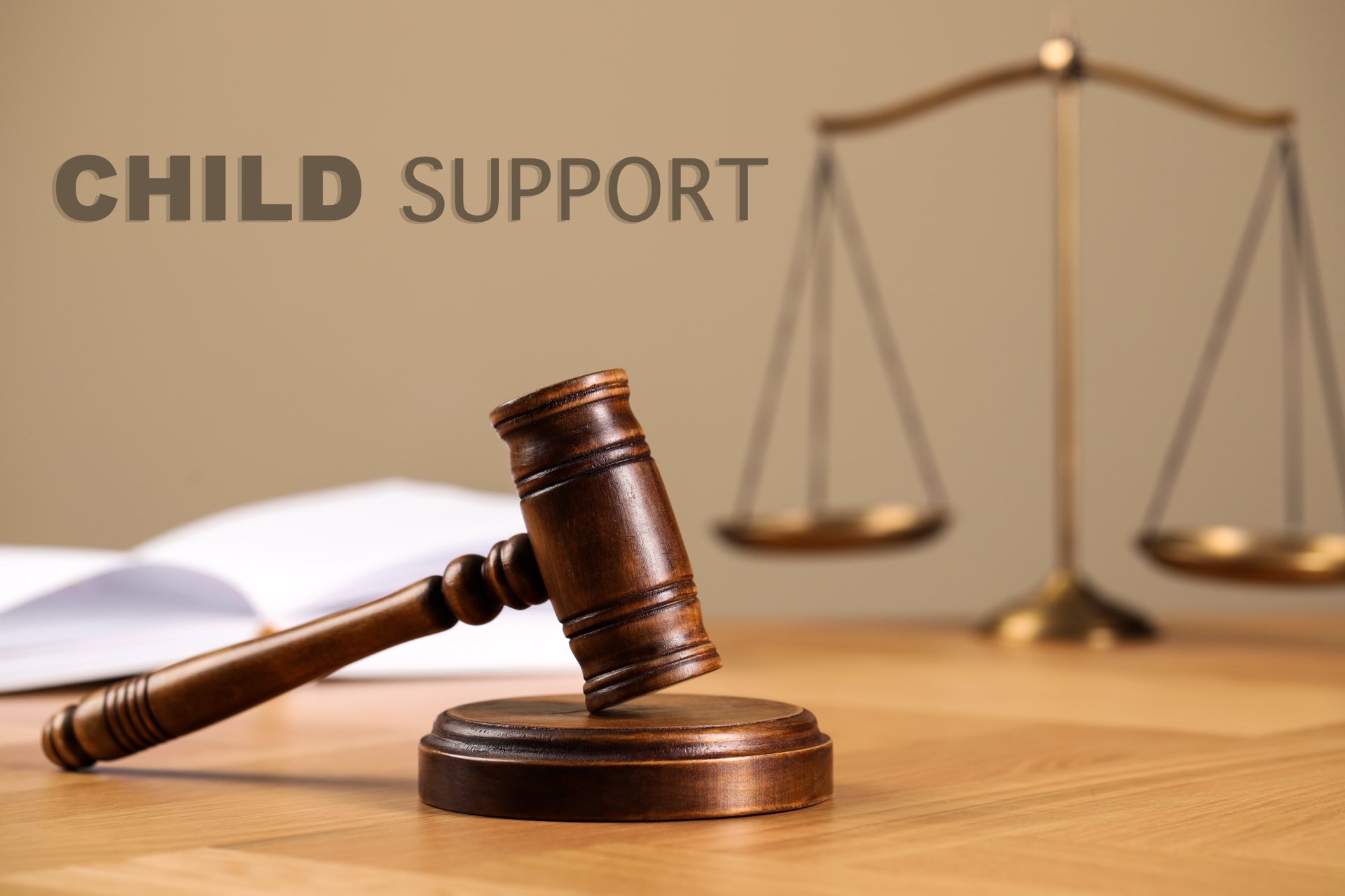 Wooden gavel, open book and scales of justice on table with child support written