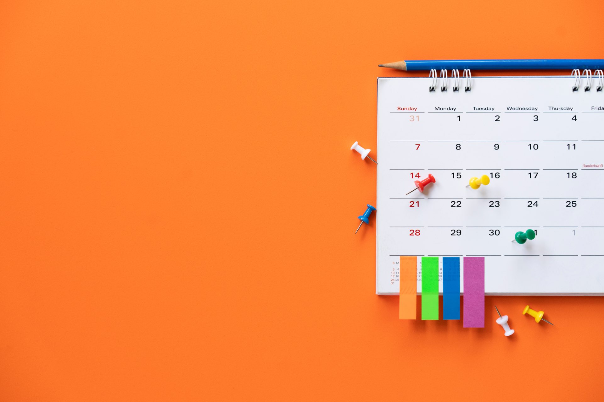 Close up of calendar with sticky notes and thumbtacks on orange background