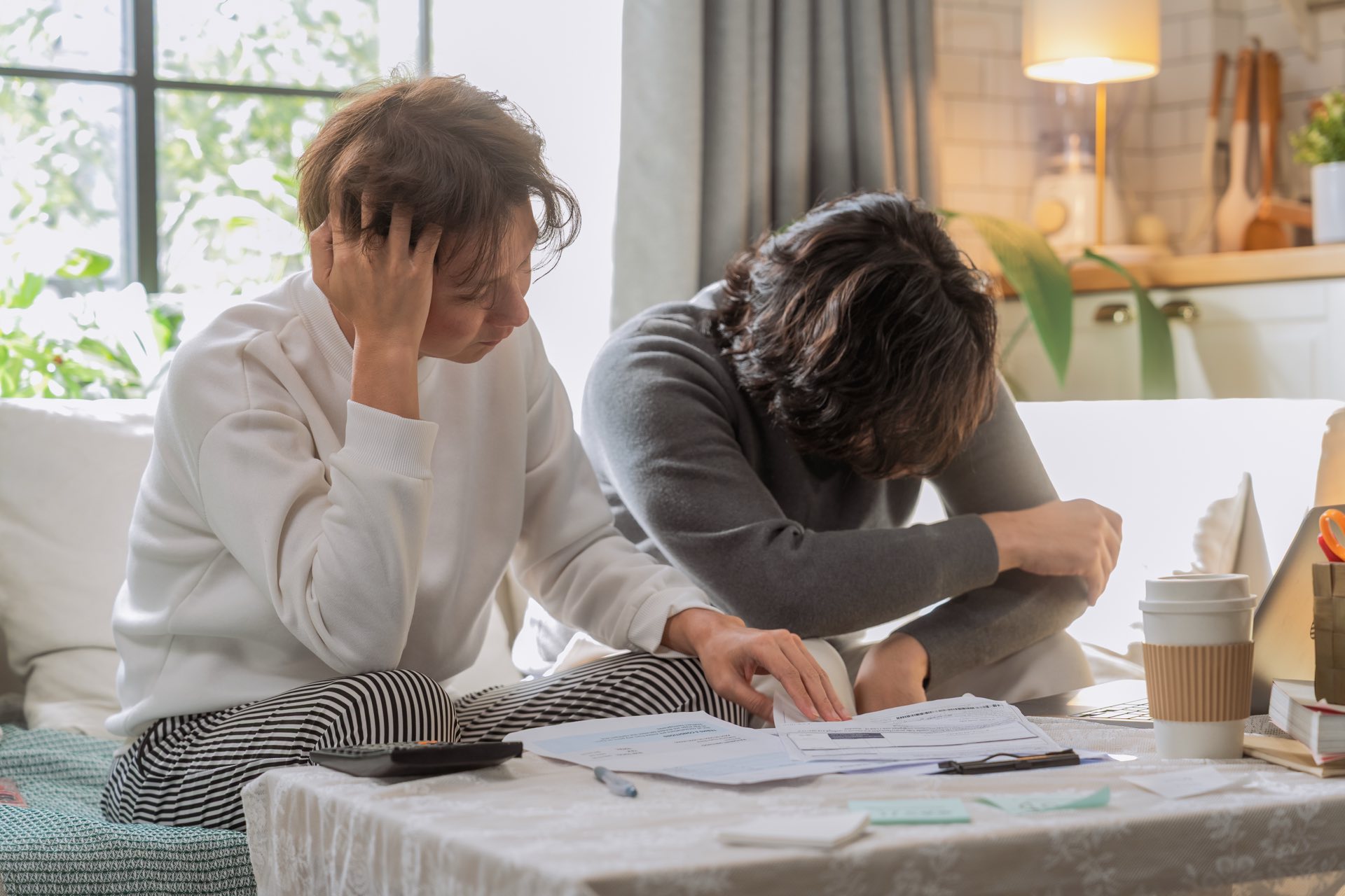 Two people sitting on a couch and looking stressed going over paperwork