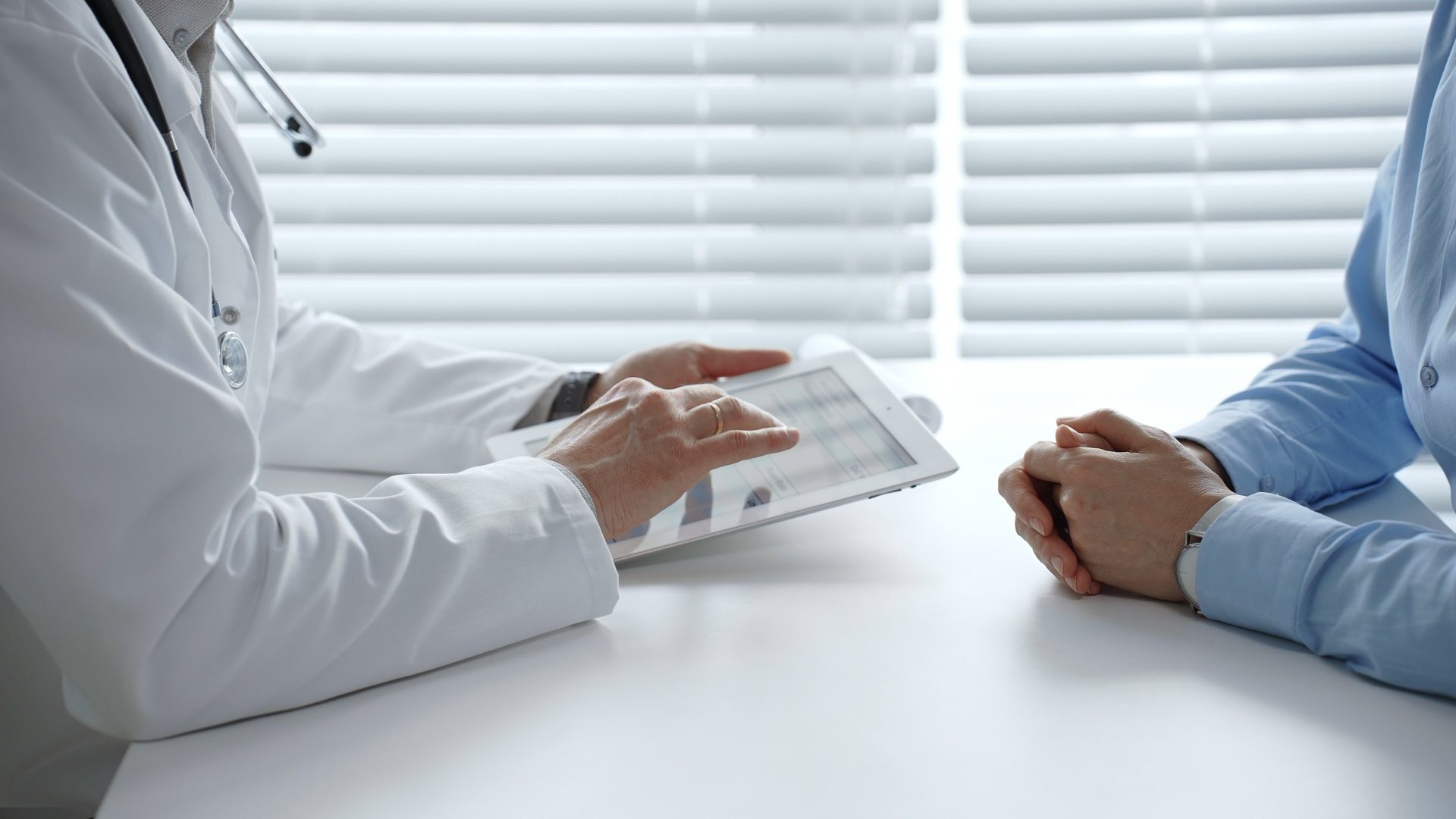 A doctor wearing a stethoscope sitting at a desk across from another person going over paperwork