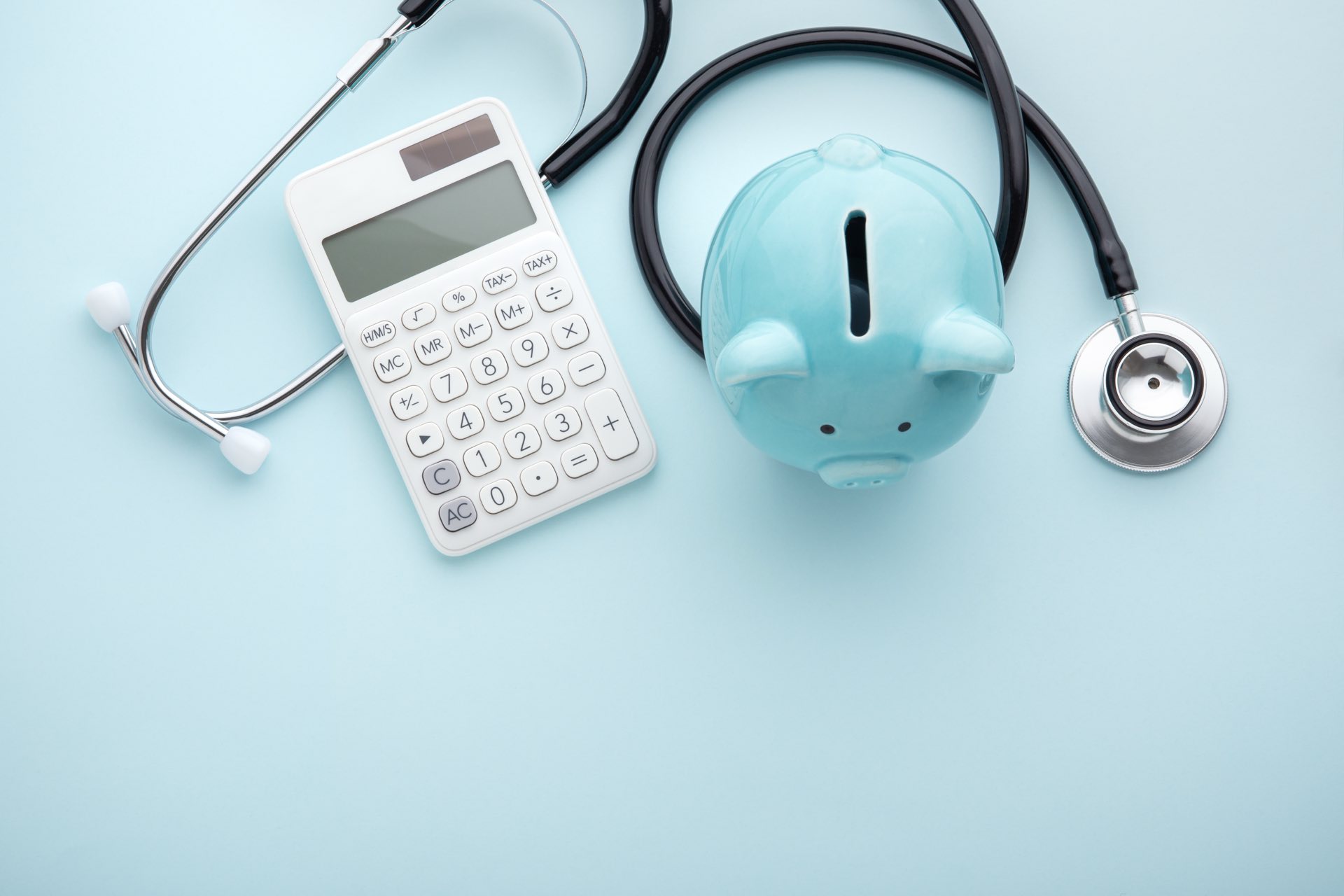 A piggy bank, stethoscope and calculator on a blue background