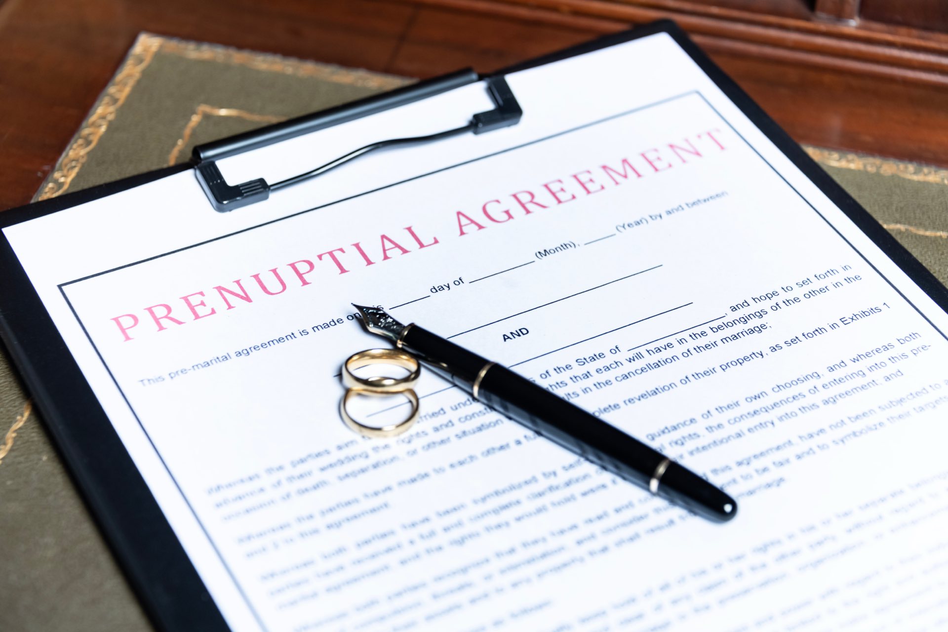 Close up of prenuptial agreement paperwork on a clipboard with a pen and two rings on top