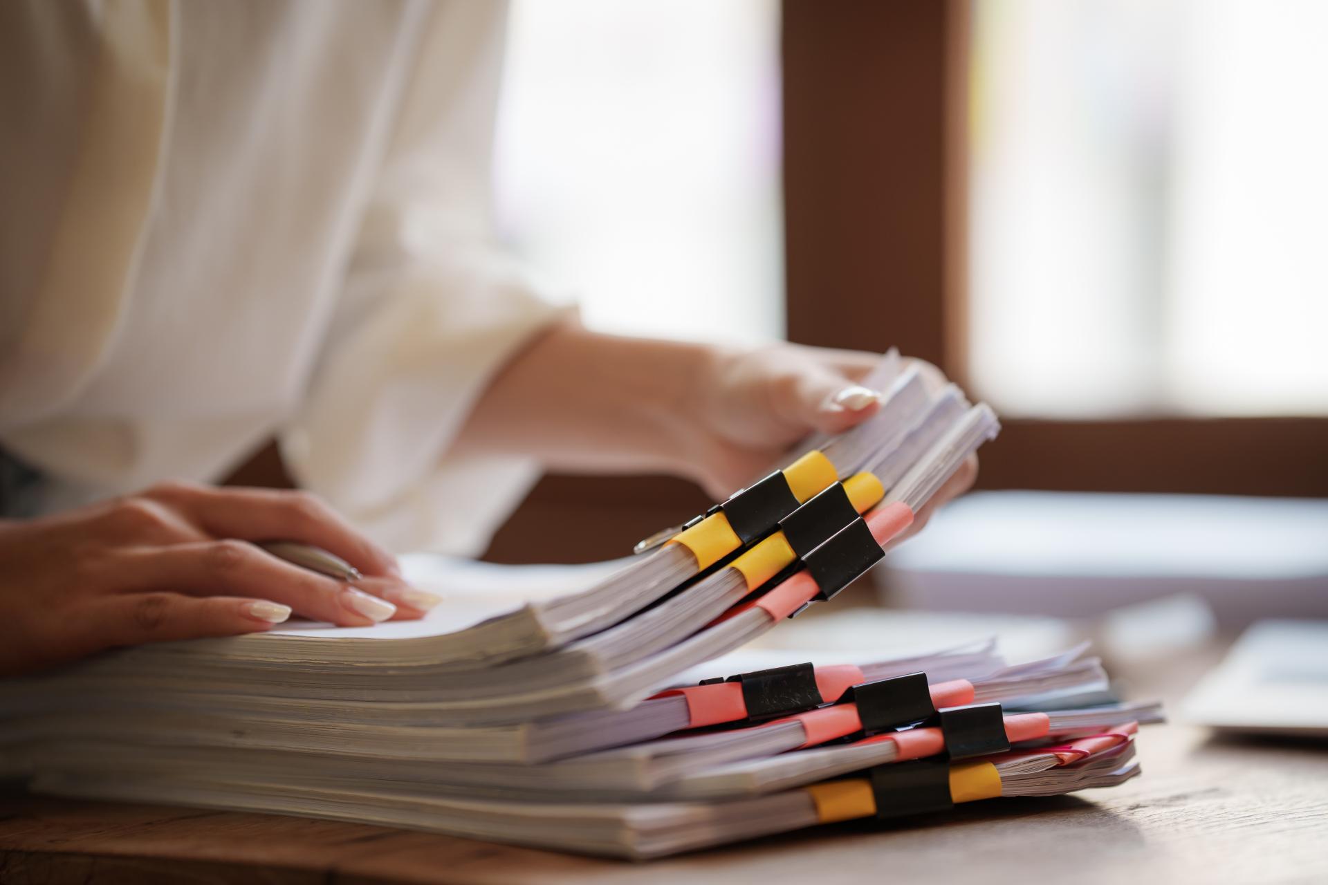 A woman looks through various stacks of papers on a desk.
